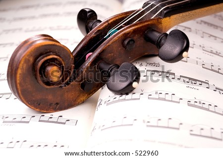 The dusty scroll of an old violin rests in the middle of a musical score. Only one line of music is in focus.