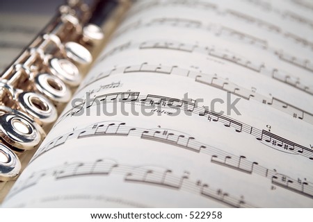 A used flute lies along the spine of an open musical score. Only one line of music is in focus.