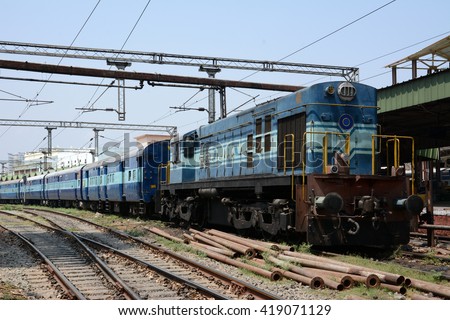 A diesel locomotive hauling a passenger train through a railway station in India.