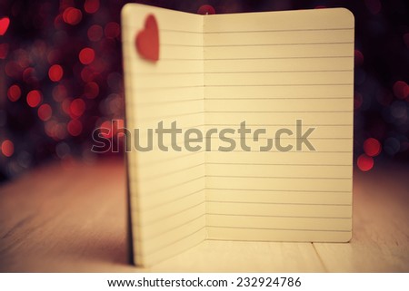 Open notebook with red heart against defocused lights, warm color toned