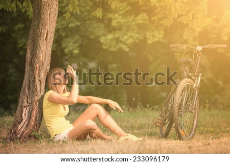 Beautiful young woman is drinking a water after cycling in sunny summer day in city park