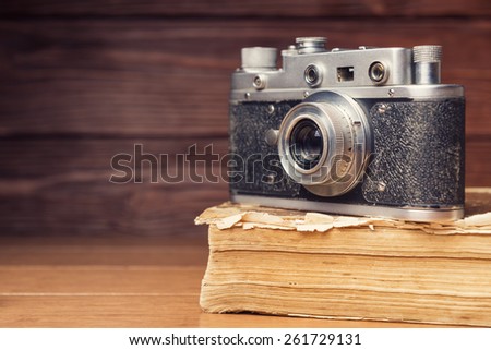 Vintage 35mm film camera on old book over wooden defocused background