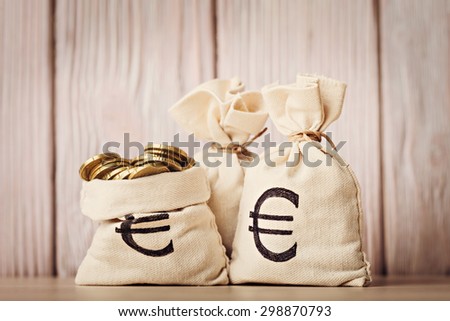 Money bags with euro coins over defocused wooden background