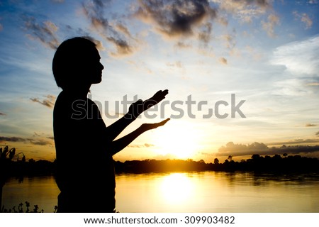 silhouettes Women praying hand over beautiful sun set background.
