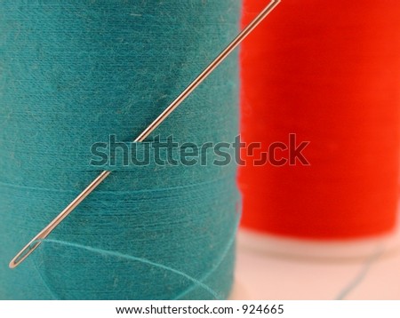 threaded needle in blue spool of thread with red spool in background