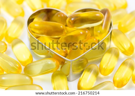 Fish oil pills on heart shape box among piles of fish oil pills isolated on white background