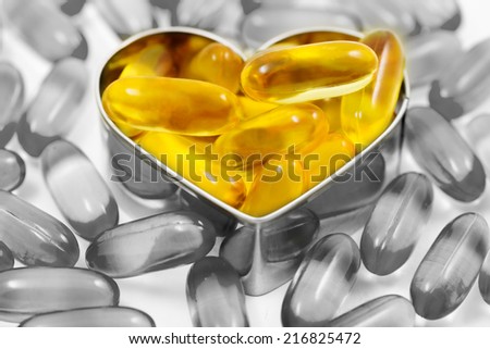 Fish oil pills on heart shape box among piles of fish oil pills black and white isolated on white background split tone