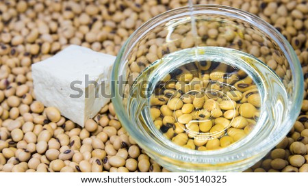 Soybeans oil poured on glass bowl with tofu on soybeans background