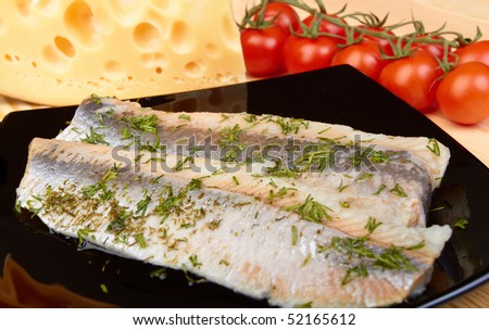 Herring on black plate with piece of cheese and tomato cherry on wood board