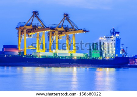 Container Cargo freight ship with working crane bridge in shipyard at twilight Container Cargo freight ship with working crane bridge in shipyard at twilight