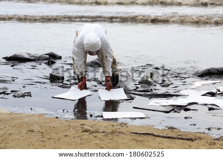 Rayong, Thailand - July 31, 2013: A Worker in biohazard suit placing absorbent paper in a clean-up operation of crude oil spilled at Ao Prao Beach on July 31, 2013 in Koh Samet, Rayong, Thailand.