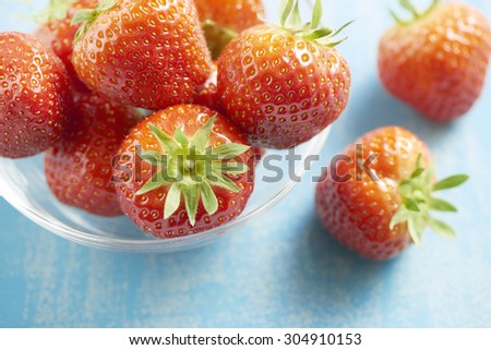 fresh healthy and tasty strawberries served in a glass bowl on a blue table. Some strawberries fallen out of the bowl.