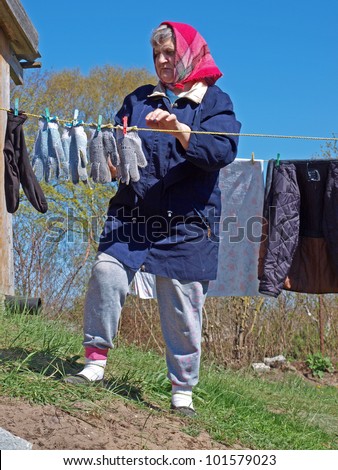 Senior woman in country yard hanging clothes on rope
