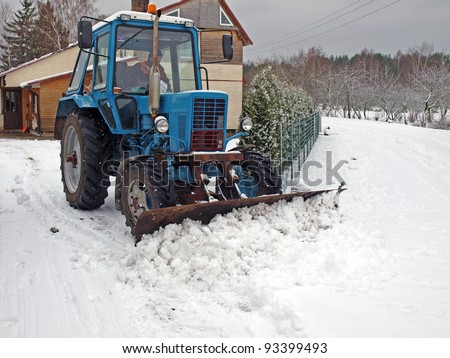 Tractor plowing snow on country yard and road