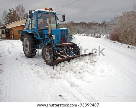 Tractor plowing snow on country yard and road