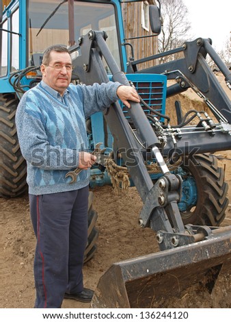 Senior farmer repairing tractor, holding the wrench