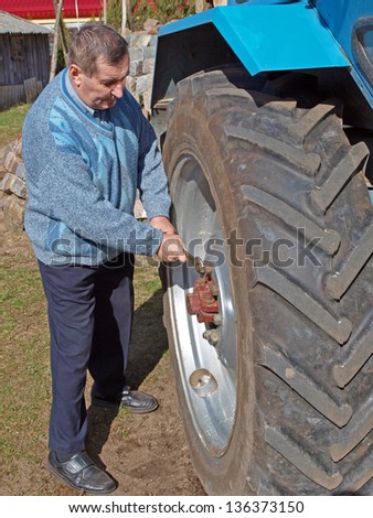 Senior farmer repairing tractor, holding the wrench