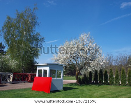 Country yard with blooming plum tree, white cabin and red metal sheets