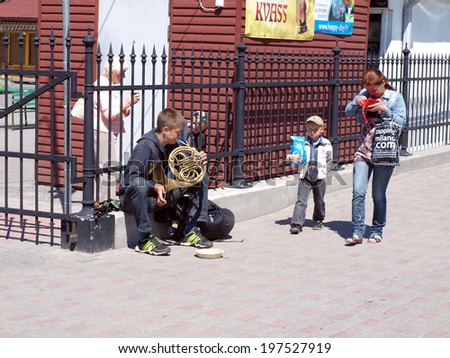 LIEPAJA, LATVIA - JUNE 8, 2014: Young street musician sits and plays the French horn to earn some money.