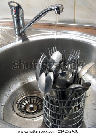 Spoons and forks in sink under water jet
