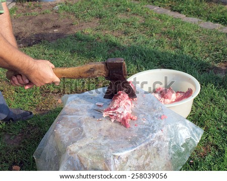 Chop the meat with an ax on wooden log outdoor