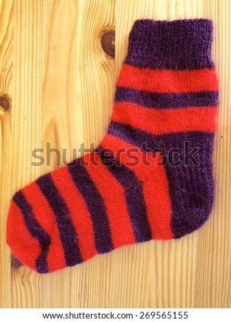 Purple and red color striped woolen sock on wooden surface vertical