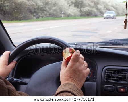 Car driver holding an apple near steering wheel