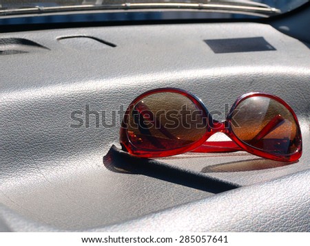 Sunglasses with brown glasses and red plastic frame on black leather car front window panel