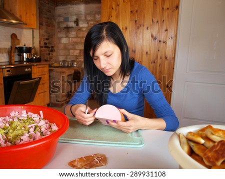 Young woman in country kitchen prepares boiled sausage for meat salad.