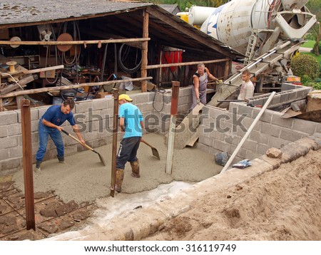 NICA, LATVIA - SEPTEMBER 14, 2013: Workers are filling foundation ditch with liquid concrete from big mobile truck cement mixer to make the cellar floor.
