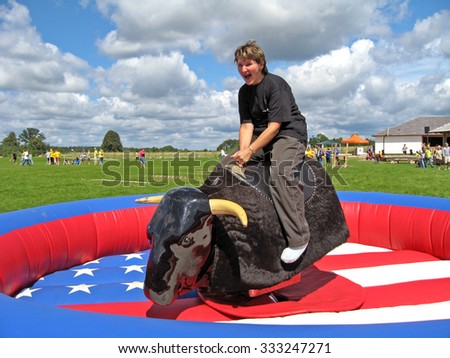 OGRE, LATVIA - JULY 14, 2007: Camping guests have a variety of sports activities. Woman is sitting on jumping artificial electric buffalo back.