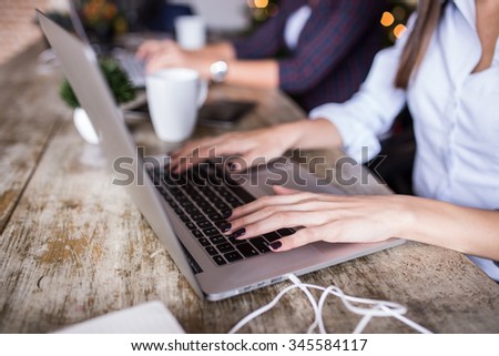Young woman using laptop at home office. Modern office interior, wooden table, close up of her hands. Depth of field