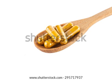 Turmeric capsules on wooden spoon isolated on white background