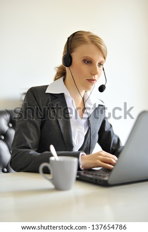 business styled woman on a desk behind a laptop. coffeecup in the front is out off focus