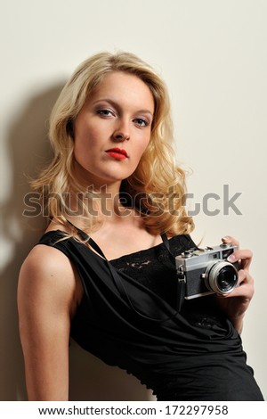 Blonde woman with long curly hair holding a vintage camera while posing for a photo. Larger depth of field.