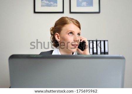 Red haired woman on the phone while sitting behind a laptop at the office. The artwork on the wall is mine, raw files will proof.