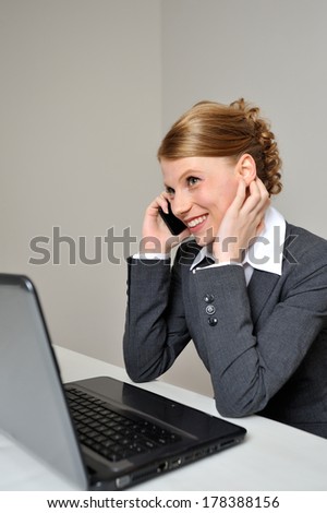Red haired business woman having a cheerful conversation on the phone. She is at work behind her laptop.