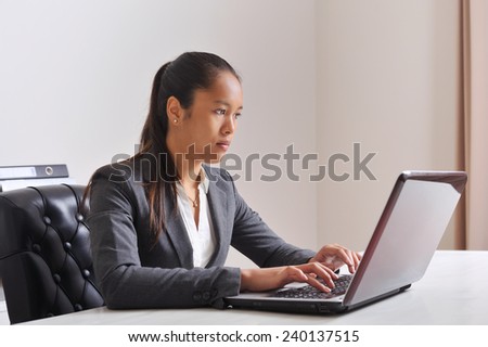 South American woman in suit at the office, working behind her laptop.