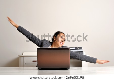 Young woman flying behind her laptop while sitting at her desk.