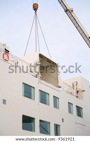 Lifting the life raft system cover off a ship for replacement of life rafts.