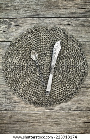 Beautiful decoration with antique tea spoon and butter-knife on handmade crochet doily. Grunge style. Sweet composition on raw wooden background.