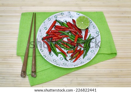 Decorative composition with chili pepper and lime on a plate and chopsticks on table-napkin over bamboo background.  Image of natural materials. Eco style.