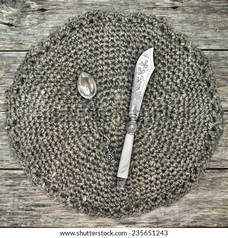 Beautiful decoration with antique tea spoon and butter-knife on handmade crochet doily. Grunge style. Sweet square composition on raw wooden background.
