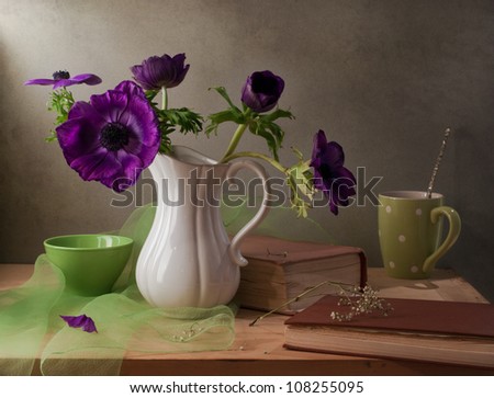 Still life with purple anemone flowers, books and cup.