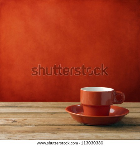 Red coffee cup on wooden deck tabletop against red grunge wall