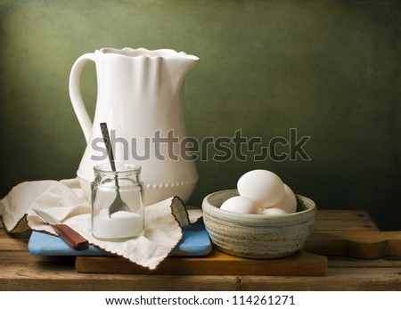 Still life with white pitcher, eggs and salt on wooden tabletop against grunge wall