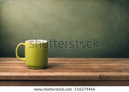 Green Mug On Wooden Table Over Grunge Background