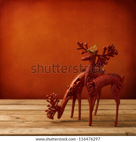 Christmas deer ornament on wooden table over red grunge background