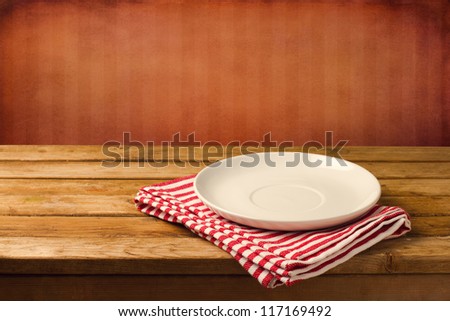 Empty White Plate On Wooden Table Over Red Grunge Background