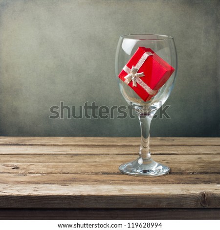Wine glass with red gift box on wooden table over grunge background